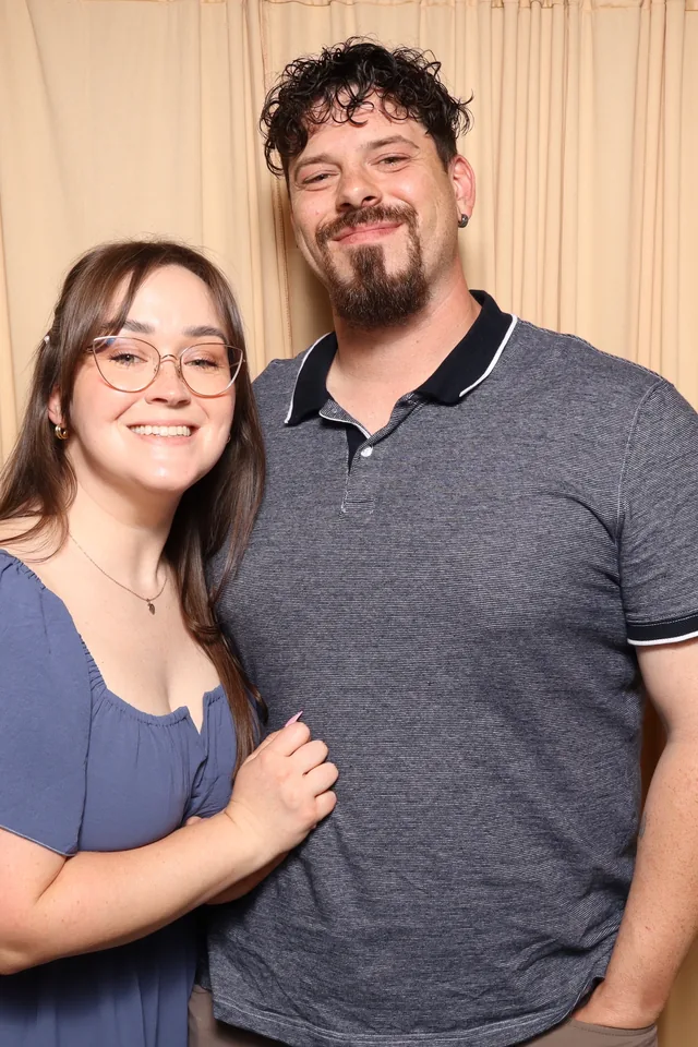 A couple posing together in front of a champagne coloured backdrop.