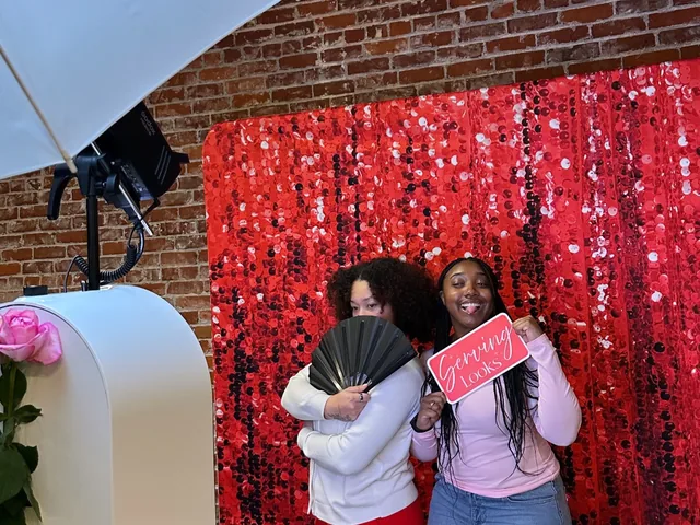 Two guests hugging in front of a red sequin backdrop.